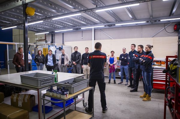 Groep mensen die luisteren naar een uitleg van een collega in operationeel uniform tijdens de introductiebijeenkomst