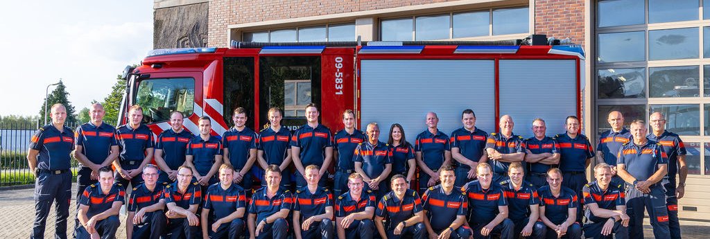 Een groep brandweermensen staat voor een brandweerwagen.
