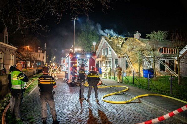 Politie en brandweermensen staan 's nachts op straat en blussen een woningbrand