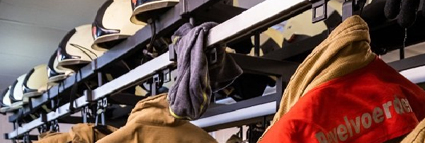 Een kapstok met brandweerhelmen en bluspakken.