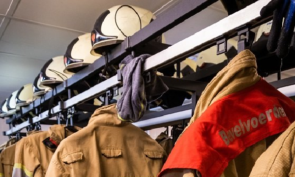 Een kapstok met brandweerhelmen en bluspakken.