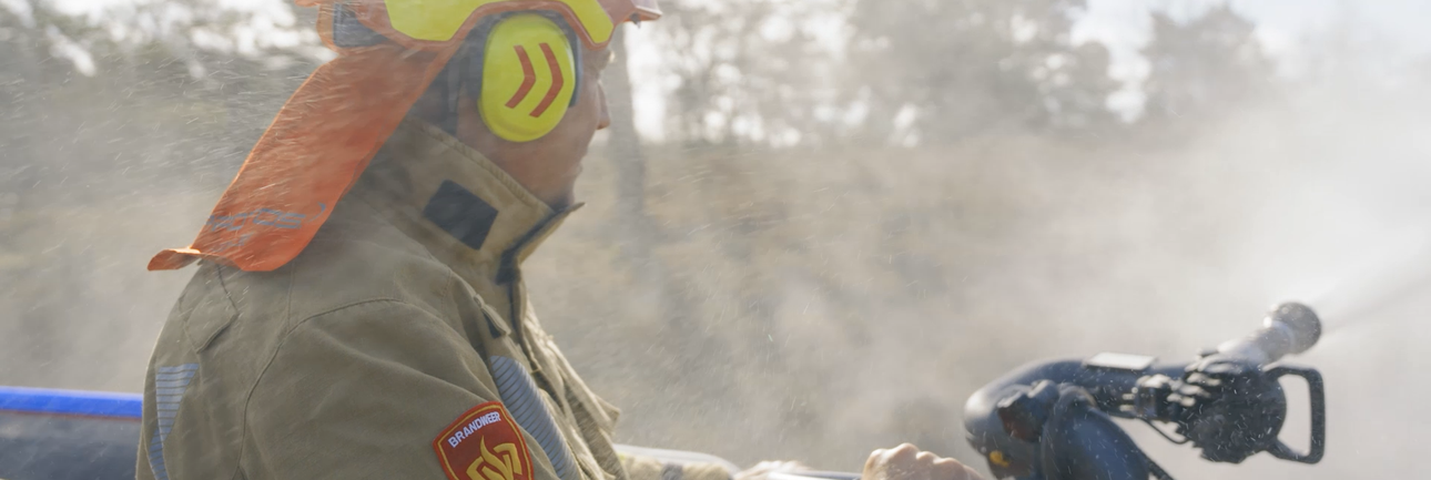 Brandweerman met brandweerkleding aan het blussen