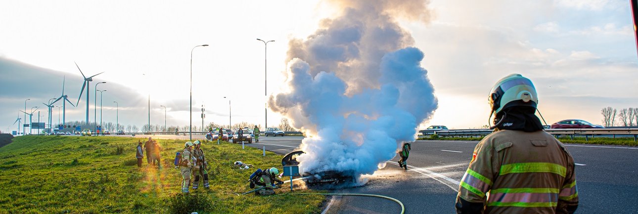 Brandweerpersoon in bluspak staat voor grote rookwolk op de snelweg