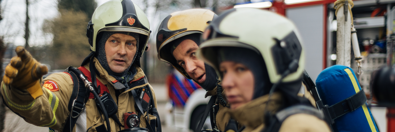 Drie brandweermensen staan buiten op een rij naar iets te kijken en te wijzen