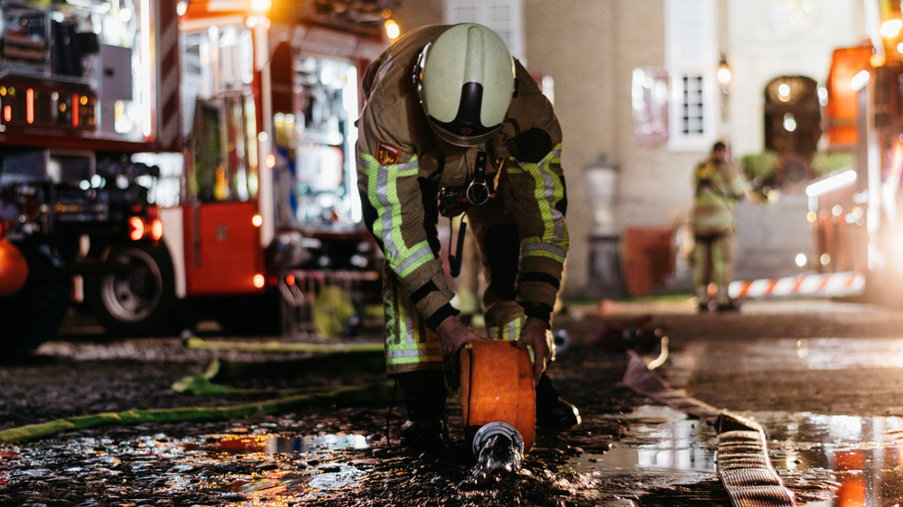Een brandweerman rolt een brandslang uit op straat