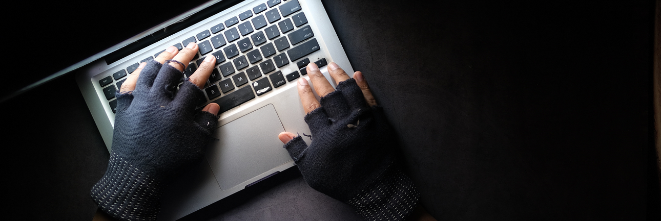 Handen in handschoenen zonder vingertoppen boven een laptop in het donker