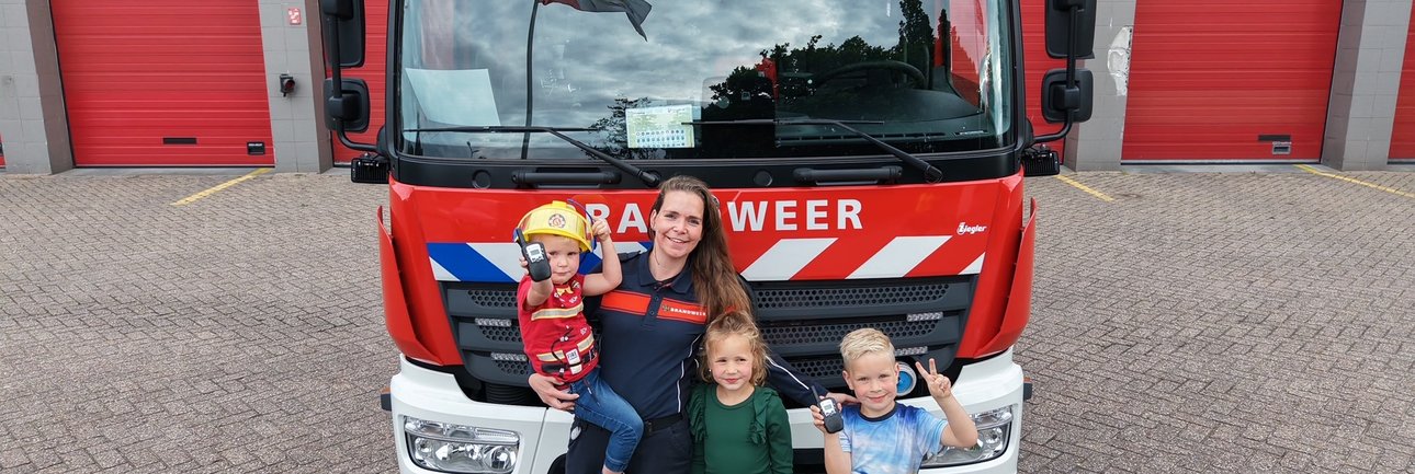 Brandweervrouw Manon poseert poseert met drie kinderen voor brandweervoertuig.