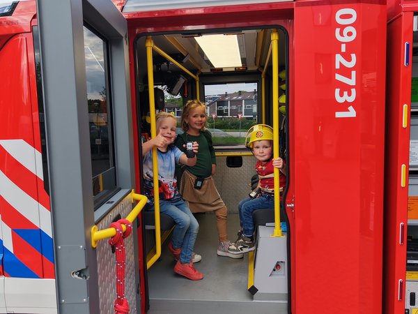 Brandweervrouw Manon poseert poseert met drie kinderen in brandweervoertuig.