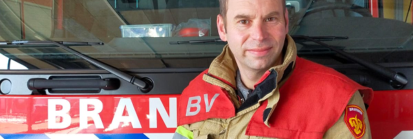 Man in bluspak geposeerd voor een brandweervoertuig