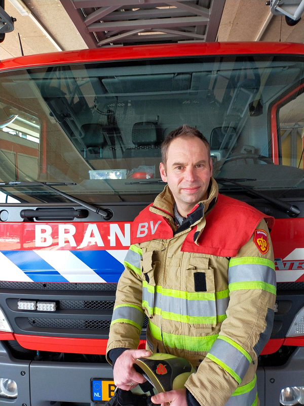Man in bluspak geposeerd voor een brandweervoertuig