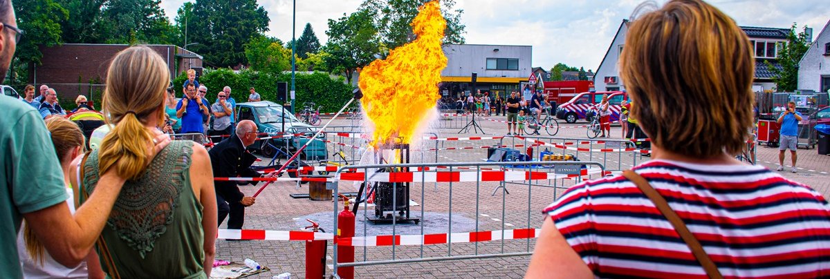 De brandweer geeft een demonstratie van het blussen van een vuurtje. Kijkend publiek.
