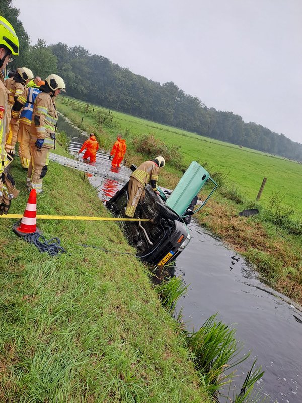 Brandweermensen halen een gekapseisde auto uit een sloot