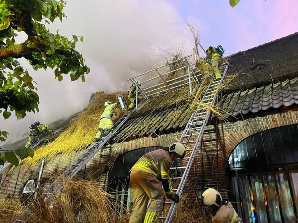 Brandweermensen in bluspak blussen brand van een rieten dak