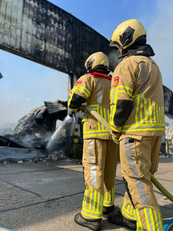 Twee brandweermensen blussen een brand in een loods