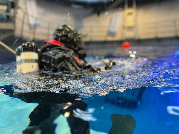 Brandweerduiker aan het wateroppervlak tijdens een duikoefening in een oefenbassin