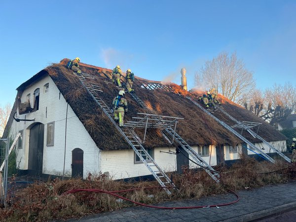 Brandweermensen in bluspak staan op een rieten dak