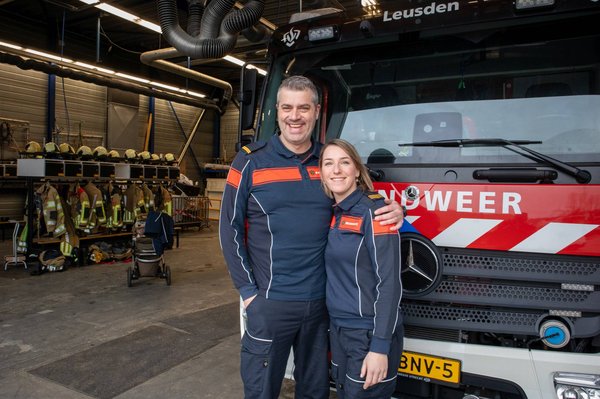 Brandweerman en vrouw die elkaar vasthouden, voor een brandweervoertuig