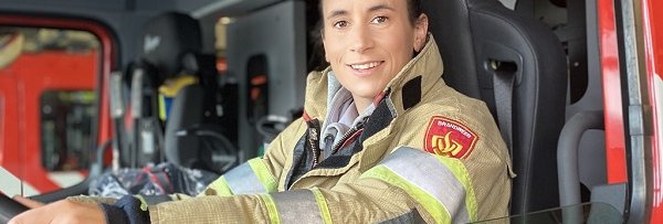 Vrouw in brandweeruniform zit achter het stuur van een blusvoertuig