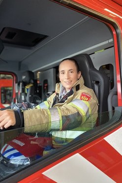 Vrouw in brandweeruniform zit achter het stuur van een blusvoertuig
