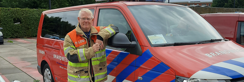 Brandweerman in blusjas naast een brandweervoertuig