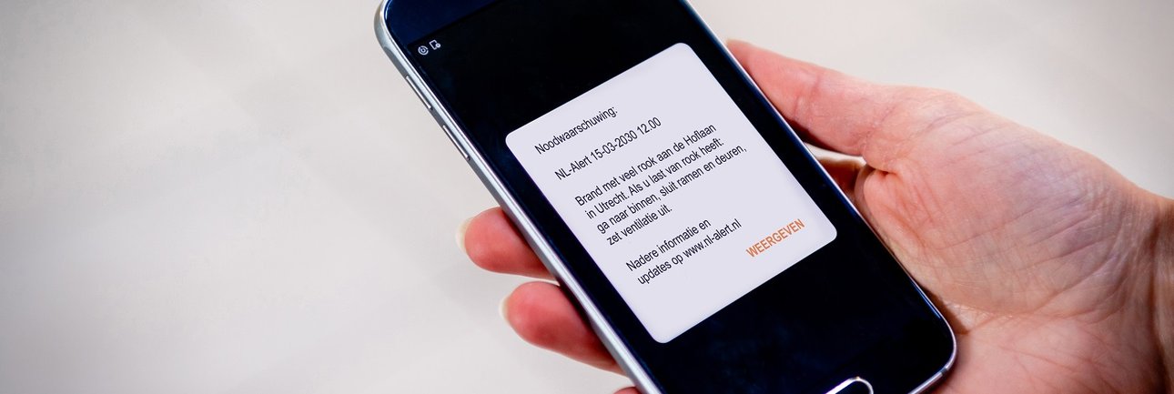 Mobiele telefoon in hand met daarop een NL-alert zichtbaar
