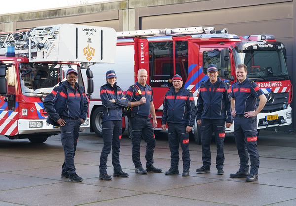 6 brandweermensen poseren voor 2 brandweervoertuigen in het nieuwe operationeel uniform