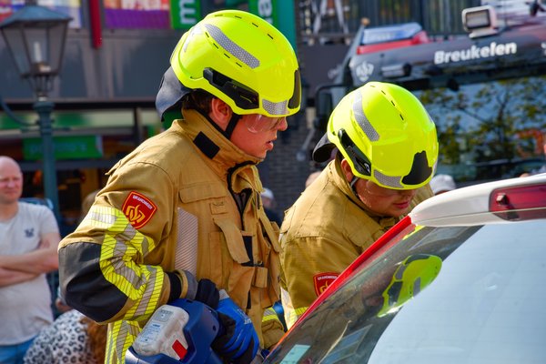 Brandweermensen in bluspak met helm op hun hoofd staan bij een auto