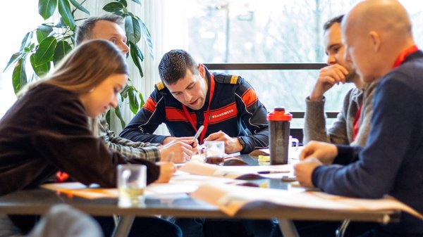 Vier mannen en een vrouw werken aan een tafel vol met papierwerk