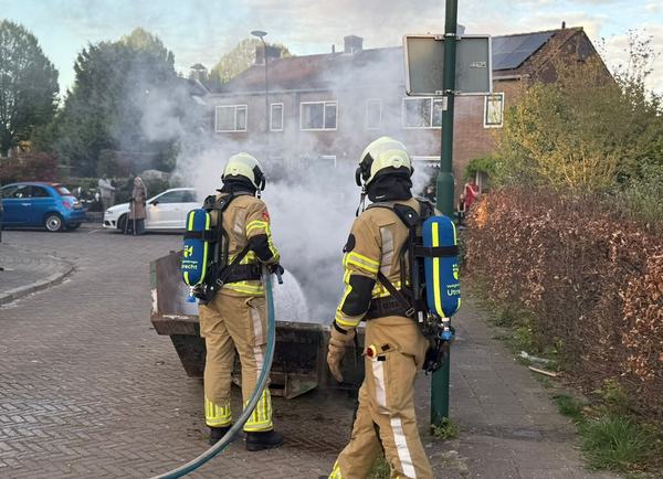 Brandweermensen blussen brand in open containerbak