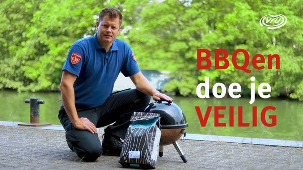 Brandweerman hurkt bij barbecue met zak kolen aan de rand van het water