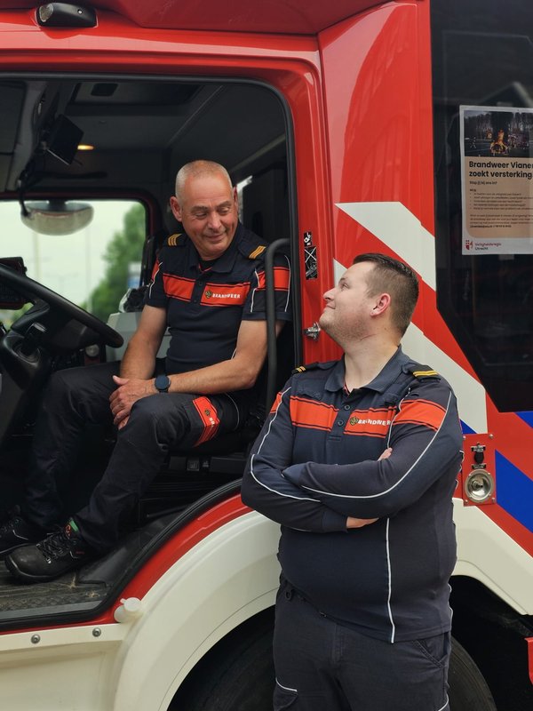 Vader en zoon, Rene en Kevin, poseren in brandweerkleding in het brandweervoertuig.