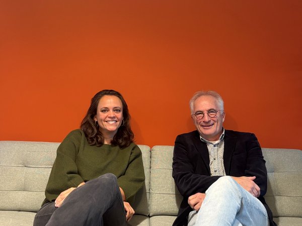 Een man en vrouw zitten geposeerd op een bank tegen een oranje muur