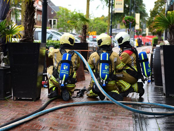 Brandweervrijwilligers knielen met een aanvalsslang tijdens een inzetoefening op straat