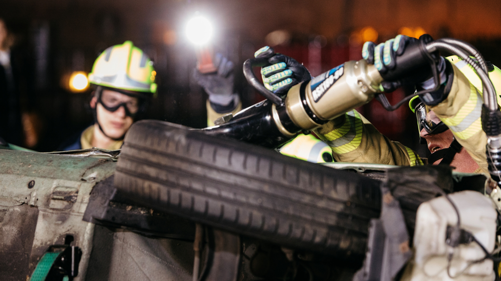 Brandweermensen openen met snijapparatuur een auto op zijn kant