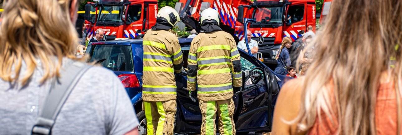 Twee vrouwen en twee brandweerpersonen staan voor een kapotte auto en brandweervoertuigen