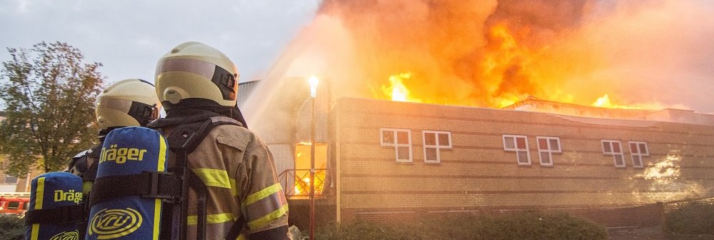 Twee brandweermannen blussen een brandend bedrijfspand