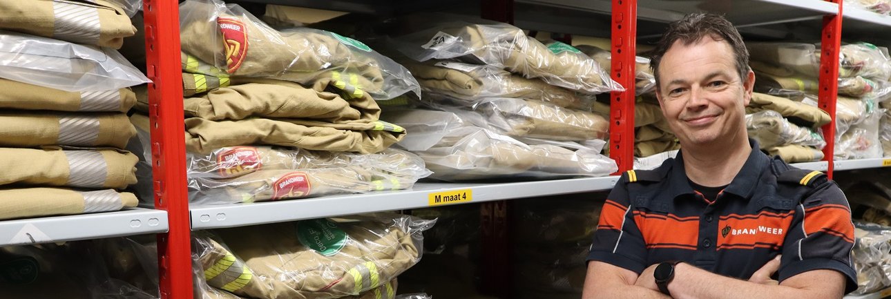 Brandweerman Marcel poseert in het magazijn van nieuwe brandweerpakken.