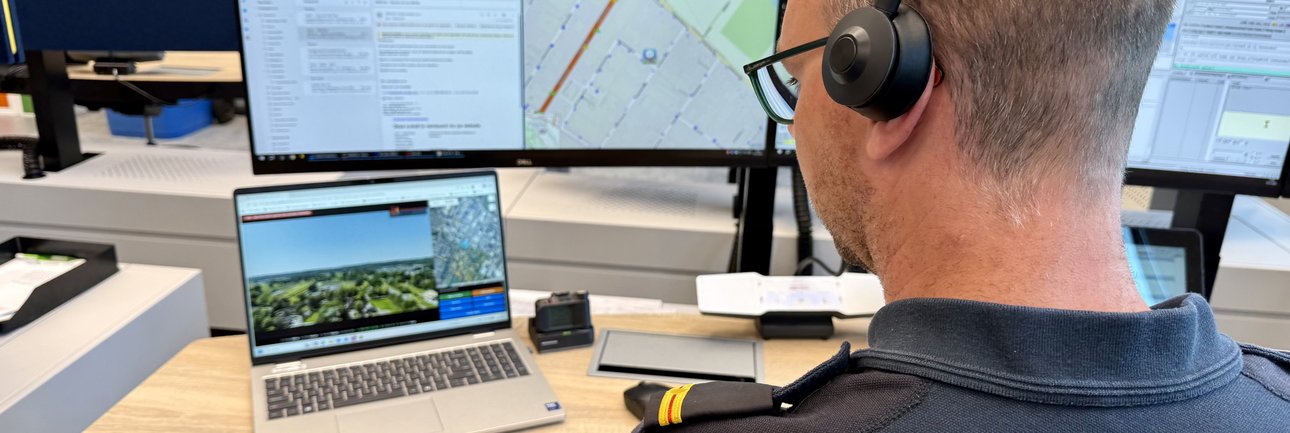 Man in brandweeruniform zit achter een bureau en kijkt naar computerschermen