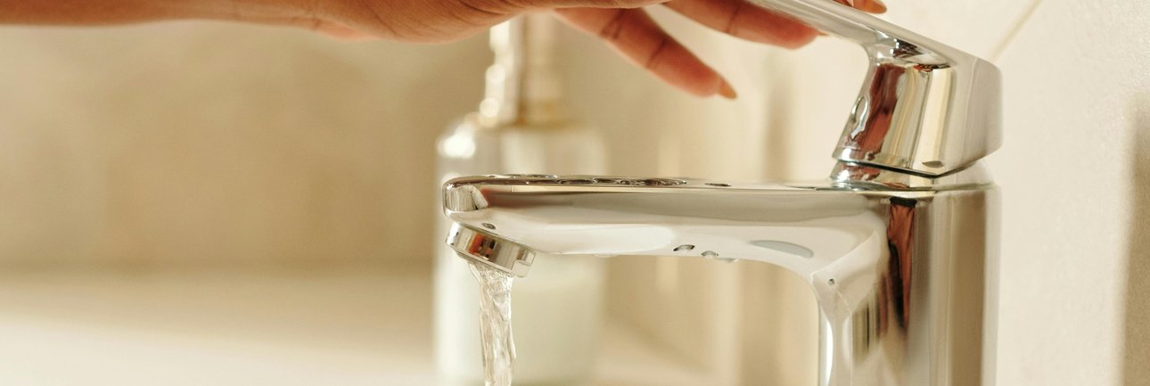 Kraan waar water uitloopt en hand die op de kraan zit