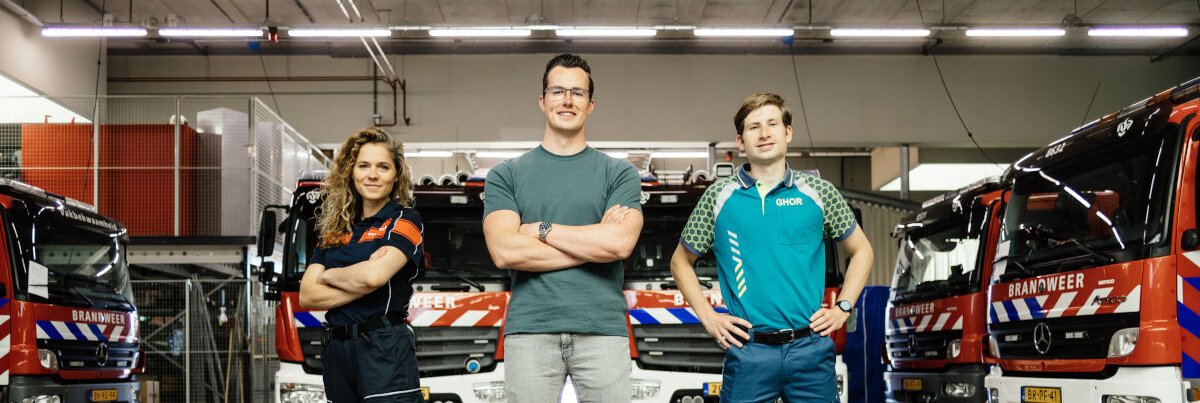 Drie mensen staan voor verschillende brandweervoertuigen