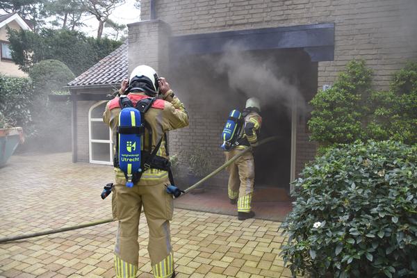 Brandweermensen gaan gebouw binnen waar rook uit komt