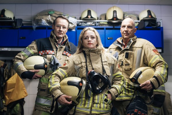 Drie brandweervrijwilligers in uniform staan in de remise