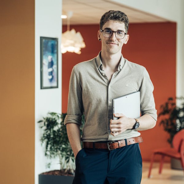 Jonas Geusebroek staat met laptop in zijn arm in een warm uitziende kantooromgeving